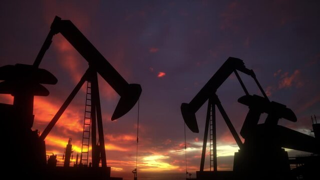 Oil pumps working at sunset on oil field, silhouettes of oil pump jacks mining energy from underground.
