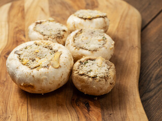 Stuffed mushrooms cups on a wooden board and table. High quality product with breadcrumbs, cheese and herbs ready for oven cooking.