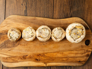 Stuffed mushrooms cups on a wooden board and table. High quality product with breadcrumbs, cheese and herbs ready for oven cooking.