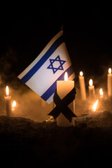 Israel flag on burning dark background with candle. Attack on Israel, mourning for victims concept...