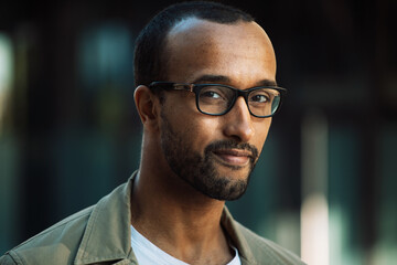 A young unshaven afro american smiling man wearing eyeglasses on the street.
