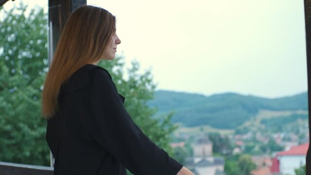 beautiful young woman on the balcony of a country house in Romanian mountains admiring beautiful landscape on background at sunset
