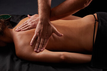 handsome male masseur giving massage to girl on black background, concept of therapeutic relaxing massage