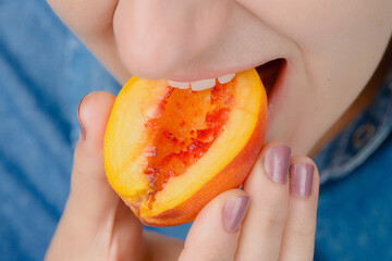 Close-up of the mouth of a Caucasian woman eating a nectarine while holding it in her hand. High angle view. Indoors.