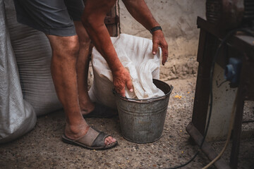 An elderly man pours wheat from a bag into a bucket.