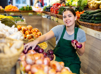 Saleswoman near fruit and vegetables stalls offering to buy red onion