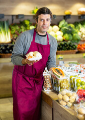 Obraz premium Male salesman near fruit and vegetables stalls offering to buy packages of carrots and papaya