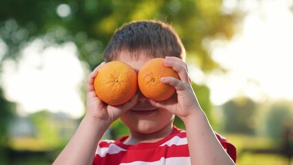Boy kid plays with fresh juicy oranges. Cute child is holding orange slices like orange glasses.Concept of healthy eating for child. Fruit vitamins for kid boy from garden. Happy family. Healthy food