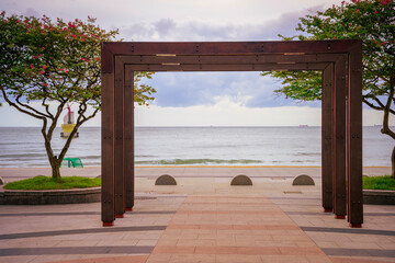 Busan Haeundae Beach Shoreline Walkway with rectangular wooden entrance frames and Zinnia flower trees with red blossoms and green foliage in Busan City, Kyongsang Namdo, South Korea