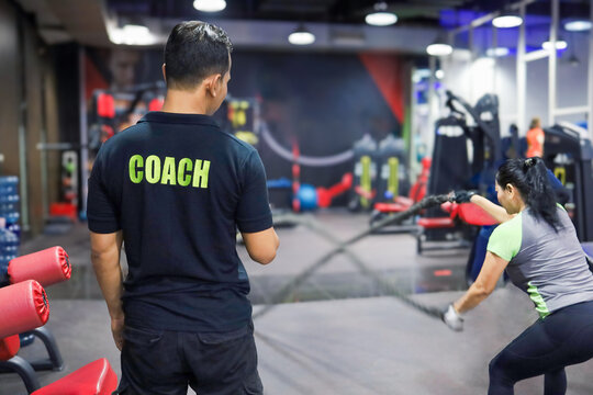 personal trainer accompanies sportswoman in gym.  trainer holding stopwatch training beautiful asian woman.  practice muscle, workout, fitness and cardio