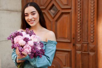 Beautiful woman with bouquet of spring flowers near building outdoors, space for text