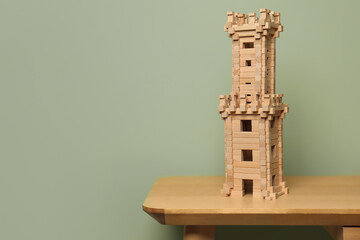 Wooden tower on table near olive wall, space for text. Children's toy