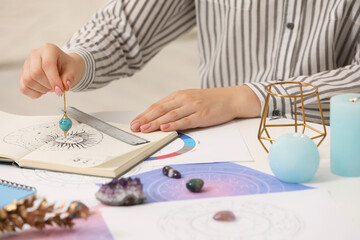 Astrologer using zodiac wheel and pendulum for fate forecast at table, closeup. Fortune telling - obrazy, fototapety, plakaty