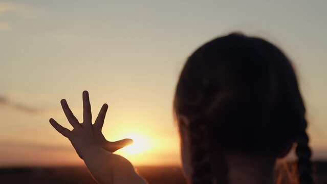 Little girl holding hand against sun silhouette in twilight summer field closeup