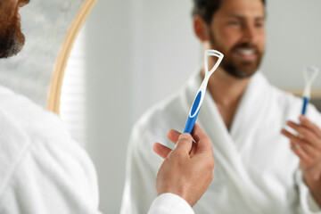 Happy man with tongue cleaner near mirror in bathroom, selective focus