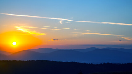 Colorful clouds in the sky at sunset against the backdrop of a mountainous forest area.