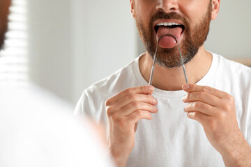 Man brushing his tongue with cleaner near mirror in bathroom, closeup © New Africa