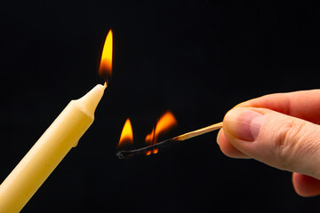 Lighting a candle with a wooden match on a dark background. Burning candle fire