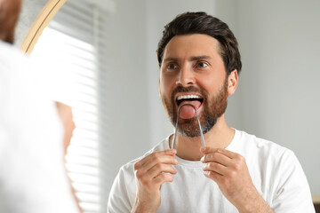 Handsome man brushing his tongue with cleaner near mirror in bathroom