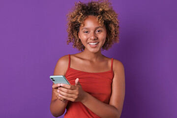 Young cheerful smiling African American woman holding phone and laughing reading SMS from boyfriend...