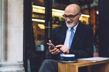 Elderly smiling businessman in glasses using smartphone against glass