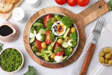 Delicious salad with pesto sauce in bowl, ingredients and fork on white table, flat lay