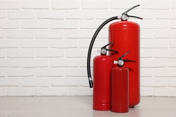 Red fire extinguishers near white brick wall, space for text