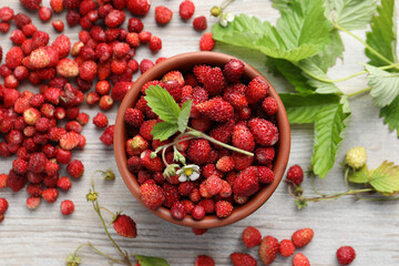 Fresh wild strawberries, flower and leaves on white wooden table, flat lay
