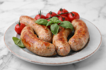 Plate with tasty homemade sausages, basil leaves and tomatoes on white marble table, closeup
