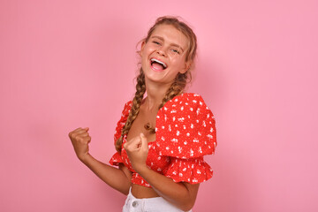 Obraz na płótnie Canvas Young cheerful positive Caucasian woman teenager makes victory gesture with both hands and laughs after learning about school team winning city championship stands on pink background.
