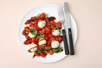 Tasty salad Caprese with tomatoes, mozzarella balls, basil and cutlery on beige background, top view