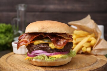 Tasty burger with bacon, vegetables and patty served with french fries on wooden board, closeup