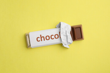 One chocolate bar in packaging on yellow background, top view