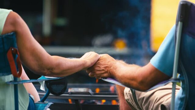 Rear view of loving senior couple camping in countryside with RV holding hands by outdoor fire - shot in slow motion
