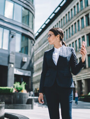 Smartly dressed businesswoman looking away from phone and standing on street