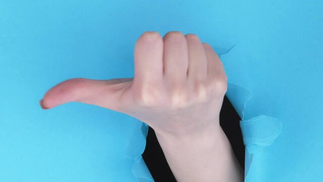 Vertical video. Vote gesture. Dislike sign. Female hand showing rejection no thumb down on blue breakthrough paper hole ripped wall background with copy space loop.