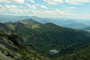 A view from the top to a small picturesque lake surrounded by high mountain ranges on a sunny summer day.