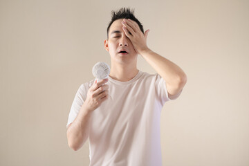 A young Asian man feels relieved when using a portable fan because of hot weather