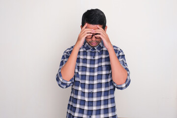 Adult Asian man looking down with hands covering his face showing stress expression