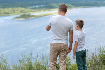 Father and son in white T-shirts walking, chatting on the riverbank on a sunny afternoon. High quality photo