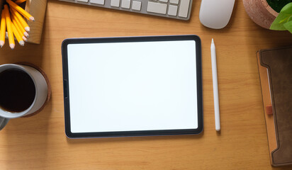 Flat lay, top view of digital tablet with white screen, coffee cup, glasses and notepad on wooden working desk.