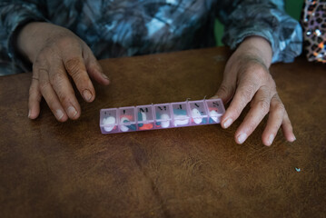 Closeup detail of elderly woman's hands organizing her medicine in a pill box.