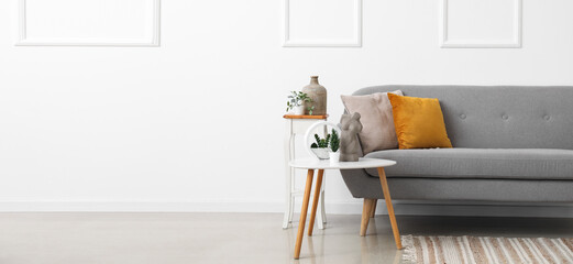 Cozy grey sofa with cushions and floral decor on tables near light wall. Banner for design - obrazy, fototapety, plakaty