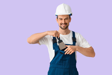 Male decorator putting putty knife in pocket on lilac background