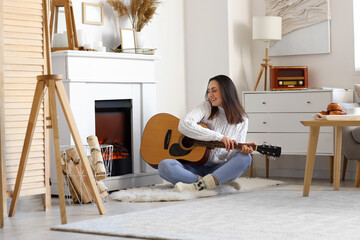 Young woman playing guitar near fireplace at home