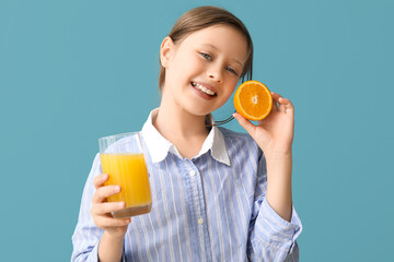 Little girl with glass of juice and orange on blue background