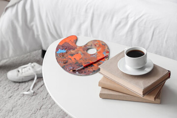 Palette, books and cup of coffee on table in children's bedroom