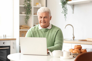 Senior man using laptop in kitchen