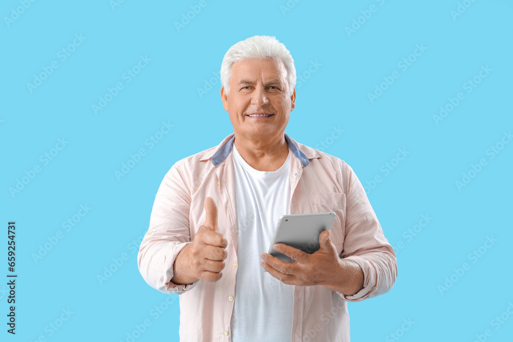 Poster Senior man with tablet computer showing thumb-up on blue background