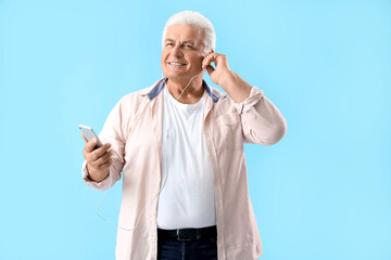 Senior man in earphones with mobile phone on blue background